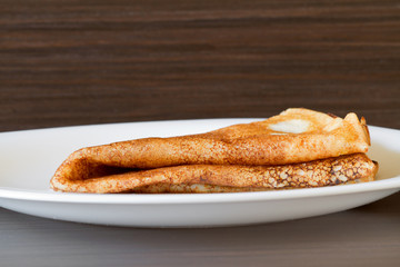 One traditional russian pancake folded triangle on a white plate on the dark background