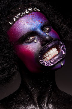 Clown and Halloween theme: Scary clown with black hair and gems, on a dark background in the studio
