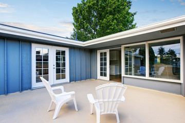 Countryside blue house with concrete floor patio area with chairs.
