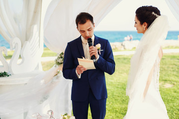 Stylish happy smiling newlyweds on the outdoor wedding ceremony