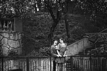 Naklejka na ściany i meble Couple hugging in love background barrier of cliff. Stylish man at velvet jacket and girl in red dress in love together. Black and white photo