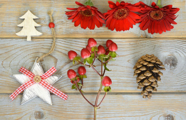 Grey wooden Christmas background with star,christmas tree, gerber daisies, pine apple and red berries twig decoration