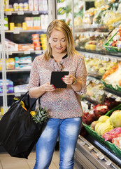 Customer Using Tablet Computer While Shopping In Grocery Store