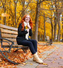 beautiful young girl portrait sit on bench in park with yellow leaf in hand, fall season, redhead, long hair