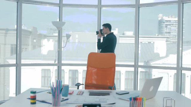 Professional photographer taking pictures with professional camera near panoramic window in modern office. 4K.