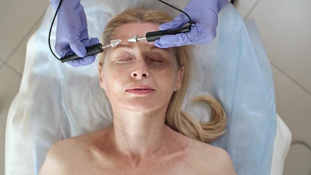 Directly above view of mature woman with closed eyes getting anti-aging treatment with  apparatus  