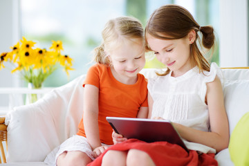 Two adorable little sisters playing with a digital tablet - obrazy, fototapety, plakaty
