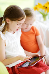 Two adorable little sisters playing with a digital tablet