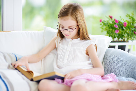 Adorable little girl reading a book in white living room