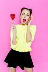 Beauty fashion model girl Eating colourful lollipop. heart-shaped Lollypop. Surprised Young funny woman with  hairstyle, pink makeup isolated on white background