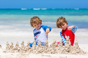 Two kid boys building sand castle on tropical beach