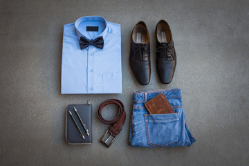 Men's casual outfits with blue jean, brown wallet, brown belt, shoes, blue shirt and bow tie on gray flat lay background