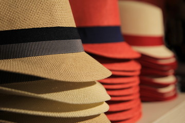 Straw hats in red and black, stacked up for sale in a store in shallow focus.
