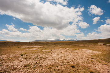 Fototapeta na wymiar Low white clouds floating over dry land of the mountain plateau in Central Asia