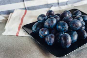 Ripe plums in a plate on a rural tablecloth and textile napkins