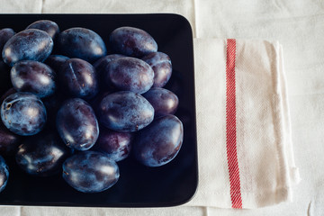 Ripe plums in a plate on a rural tablecloth and textile napkins