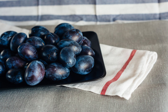 Ripe plums in a plate on a rural tablecloth and textile napkins