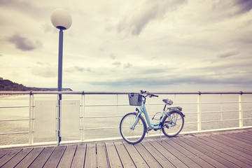 Vintage toned lonely bicycle with basket on empty pier, rainy summer day.
