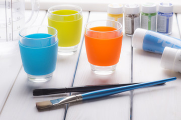 Soft still life of colorful cups, brushes and paint on a white wooden table. Drawing set.