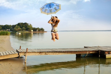 Śliczna dziewczynka skacze z parasolką do wody w jeziorze.