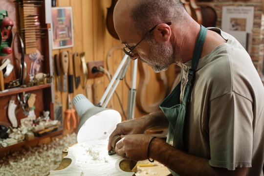 Violin maker carving and cutting on wooden corpus for new instru