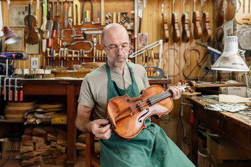 Instrument maker in his workshop checking finished violin