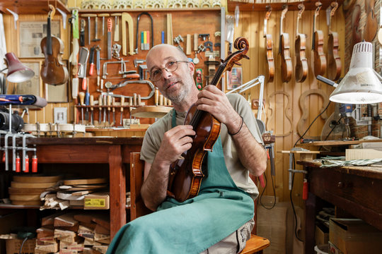 Instrument maker in his workshop checking finished violin
