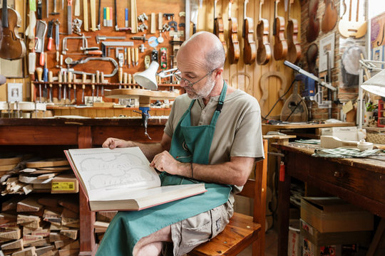Instrument maker reading book on violins