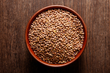 Rustic ceramic bowl of uncooked lentils isolated on dark wood from above
