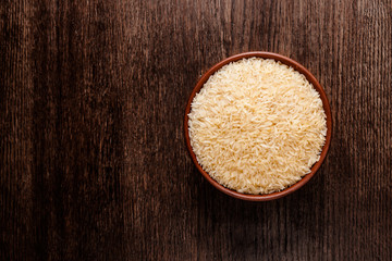 Rustic ceramic bowl of uncooked raw basmati rice isolated on dark wood from above