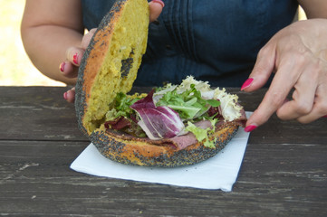 détail femme mangeant un sandwith avec du jambon et de la salade sur une table en vieux bois 
