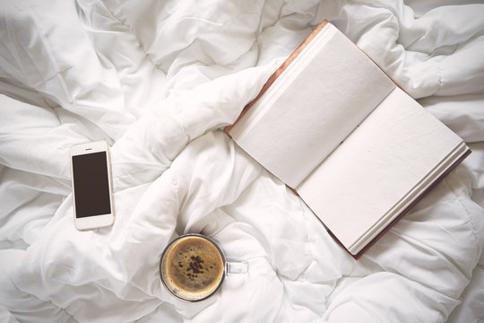 Cup of coffee, vintage notebook and smartphone on bed,