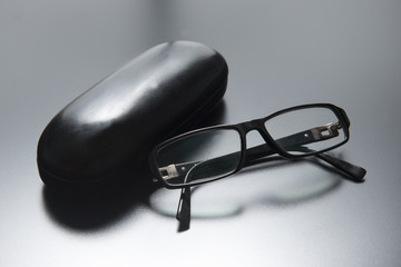 Modern black glasses on a grey reflective background