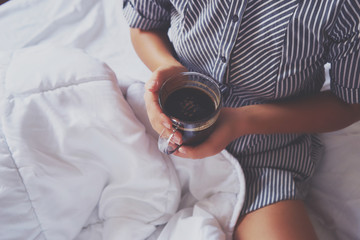 Woman hands holding a cup of hot coffee in bed