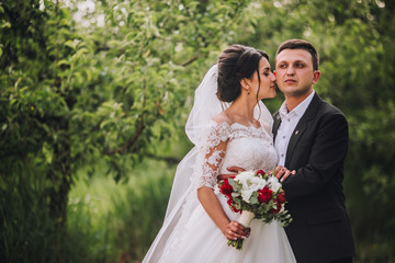 couple in wedding attire with a bouquet of flowers and greenery is in the hands against the...