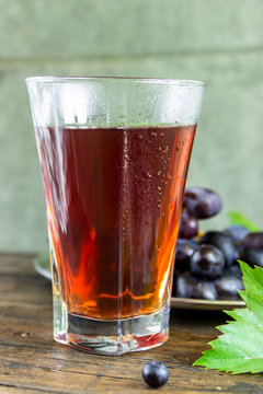 Стакан виноградного сока и кисть винограда с листьями на темном фоне. Здоровое питание