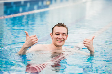 Naklejka premium Young happy man in the swimming pool gesturing thumb up