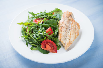Roasted chicken breast and fresh salad with tomato and greens (spinach, arugula) close up on blue wooden background. Healthy food.