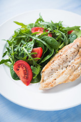 Roasted chicken breast and fresh salad with tomato and greens (spinach, arugula) close up on blue wooden background. Healthy food.