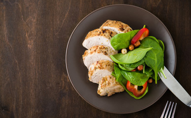 Sliced lime pork tenderloin with vegetables salad on dark wooden background top view. Space for text. Healthy food.