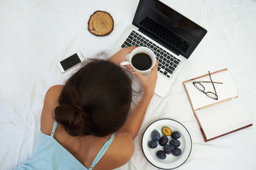 Young woman drinking coffee at home in her bed and checking her