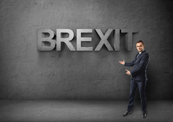 Businessman stands showing big 3d 'brexit' word by both hands on concrete background