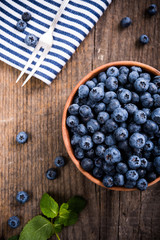 Full bowl of fresh ripe blueberries on old wooden board