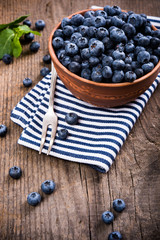 Full bowl of fresh ripe blueberries on old wooden board