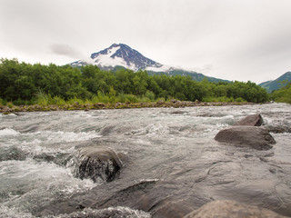 Mutnovsky Volcano on Kamchatka in Russia against the background of the brook with rocks and cloudy sky