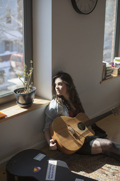 Thoughtful woman sitting with acoustic guitar near window