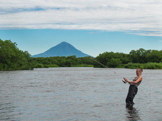 Adult woman holding a fishing pole and fish pulls against the backdrop of the river and a huge volcano Opala on Kamchatka in Russia