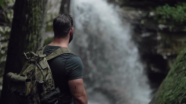 A male hiker watches a waterfall in slow motion.