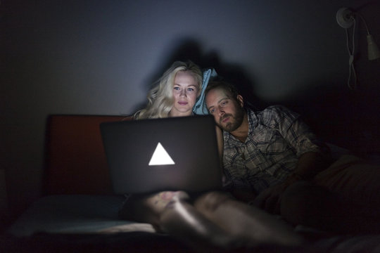 Young couple looking at a laptop in bed