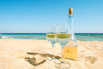 Two glasses of white wine and bottle on tropical beach. Romantic idea for couple.